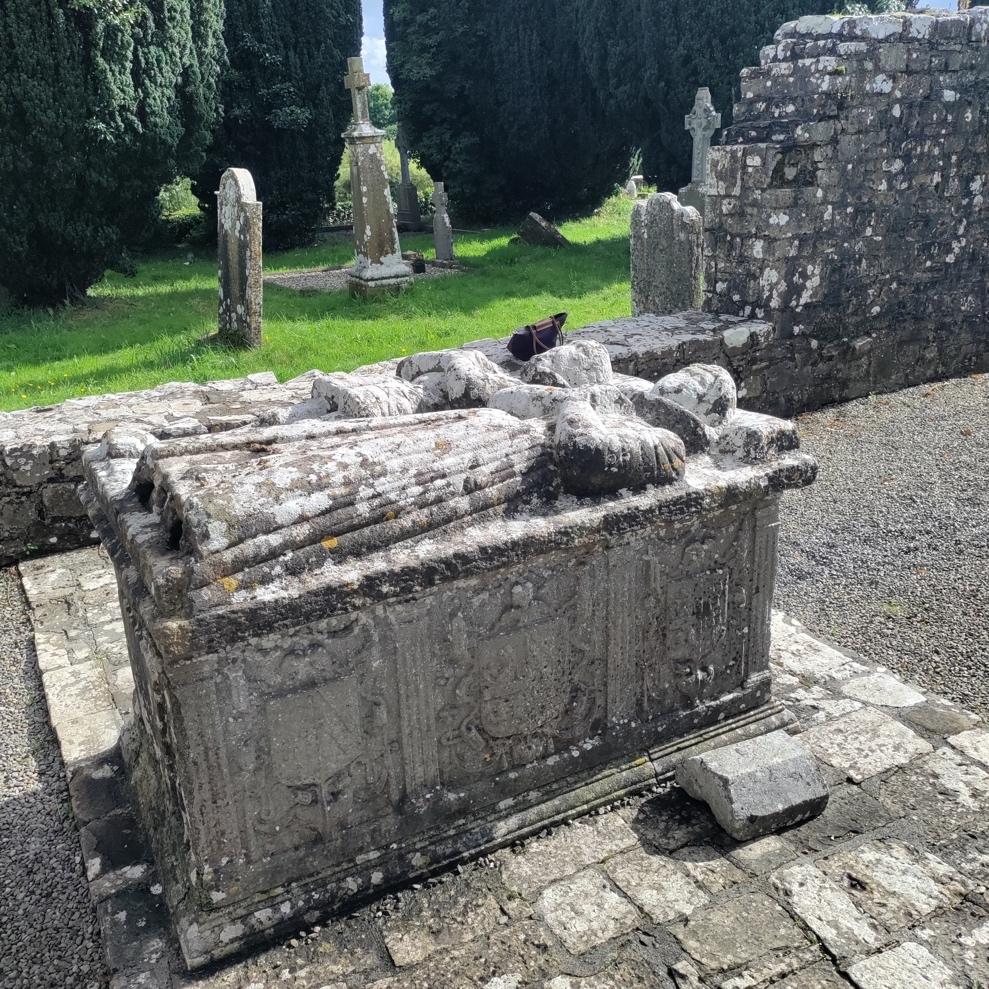 A stone tombstone with a cat in the background Description automatically generated